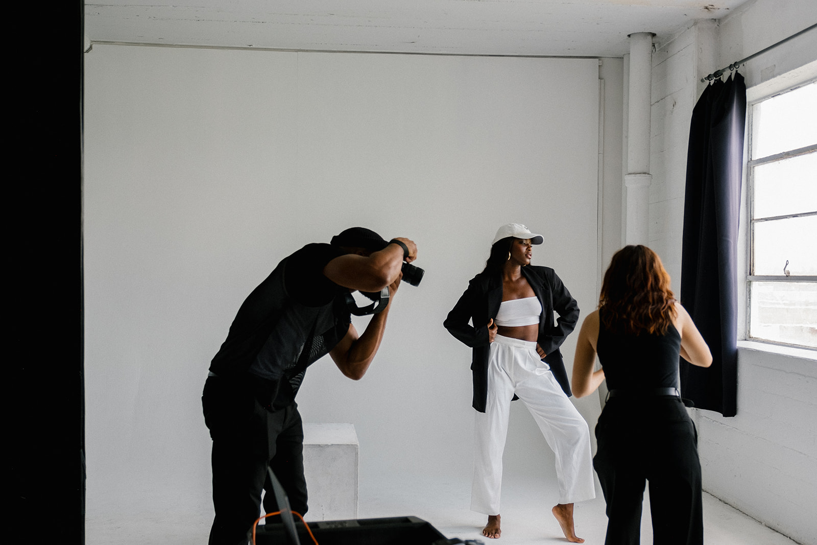 two photographers photographing one model in a white studio with natural sunlight